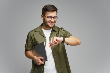 Young man checking smartwatch while holding a laptop in a modern indoor setting
