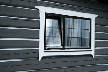 Window of grey log house covered in snow in winter season. Window is open for fresh air. Concept of need to ventilate the room in any weather.