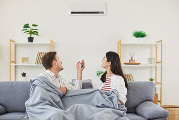 Family couple resting on sofa operates and turn on a wall-mounted air conditioner at home, focusing...