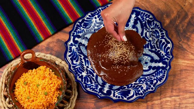 Mole poblano, traditional mexican food, hand of a mexican woman sprinkles sesame seeds on talavera dish with mole poblano and chicken