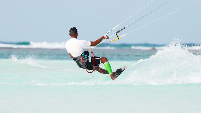 Tanned kitesurfer jumps on the water with splashes from under the board