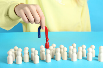 Woman with magnet attracting red piece among wooden ones on light blue background, closeup