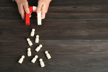 Man with magnet attracting human figures at wooden table, above view. Space for text