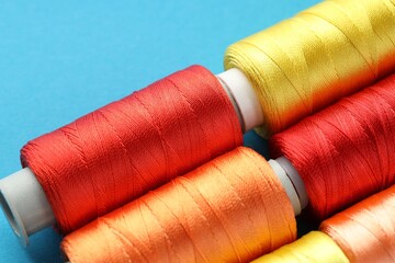 Different spools of sewing threads on light blue background, closeup