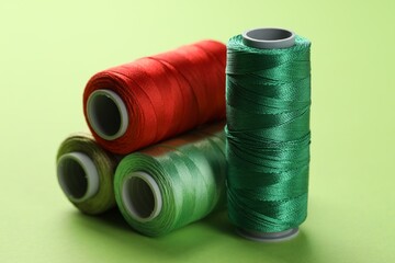 Spools of sewing threads on light green background, closeup