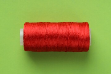 Spool of red sewing thread on light green background, top view
