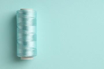 Spool of sewing thread on light blue background, top view. Space for text
