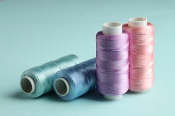 Different spools of sewing threads on light blue background, closeup