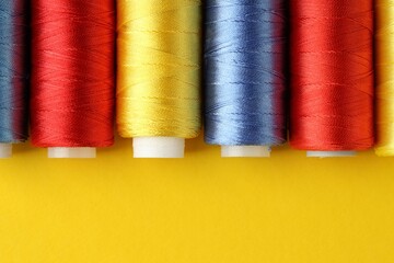 Different spools of sewing threads on yellow background, flat lay. Space for text
