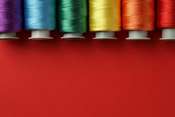 Different spools of sewing threads on red background, flat lay. Space for text