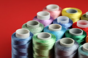 Different spools of sewing threads on red background, closeup