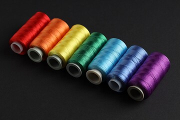 Different spools of sewing threads on black background, closeup