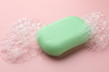 Soap bar with foam on light pink background, closeup
