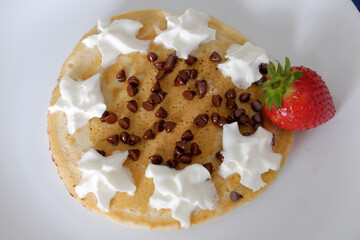 Plate with pancakes and a single red strawberry with chocolate chips and whipped cream