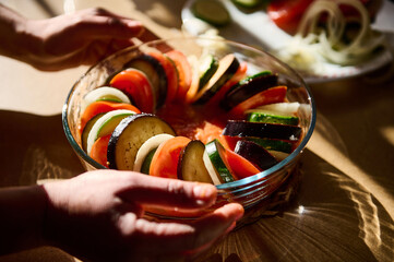 Hands arranging freshly sliced vegetables in a glass bowl during sunny day