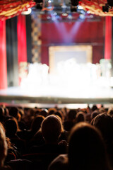 Audience at theatrical performance with red curtains and bright stage lights