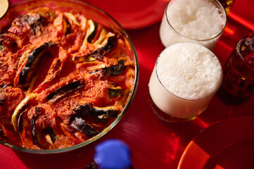 Baked vegetable dish with beer glasses on a vibrant red table