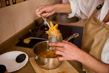 Person filling glass jar with homemade preserved vegetables in a kitchen