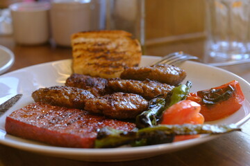 Close-up of sausages and meatballs cooked on a barbecue on a menu plate at a meat restaurant. Portion of meatballs with roasted tomatoes and green peppers. Meat prices. Food industry.
