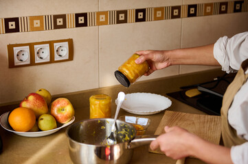 Person preserving homemade fruit jam in jars inside a cozy kitchen setting