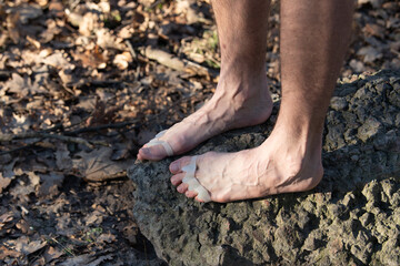 A person stands barefoot on a rock surrounded by leaves, wearing a silicone separator on their toes. The scene captures a serene moment in nature, highlighting foot care
