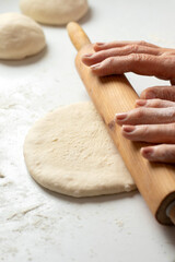 Rolling pin on dough on white kitchen table with wheat flour. Close-up. Selective focus.
