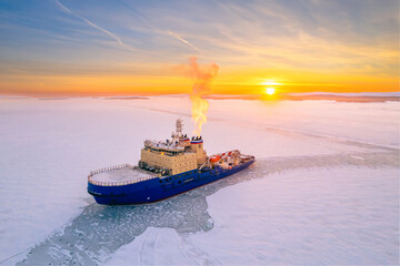 Large blue icebreaker is floating in ice, with sky behind it painted in shades of orange as sun sets in background.  © owr