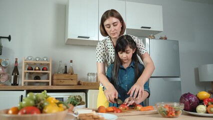Smart caucasian mother and asian girl cooking together and chopping vegetable or preparing salad for dinner. Happy mom and daughter making healthy food with fresh food. Healthy food concept. Pedagogy.