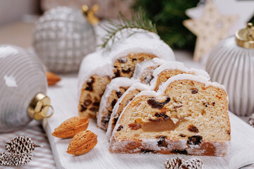 A beautifully arranged sliced stollen loaf with a powdered sugar coating, festive almonds, pinecones, and ornaments enhancing the holiday atmosphere.