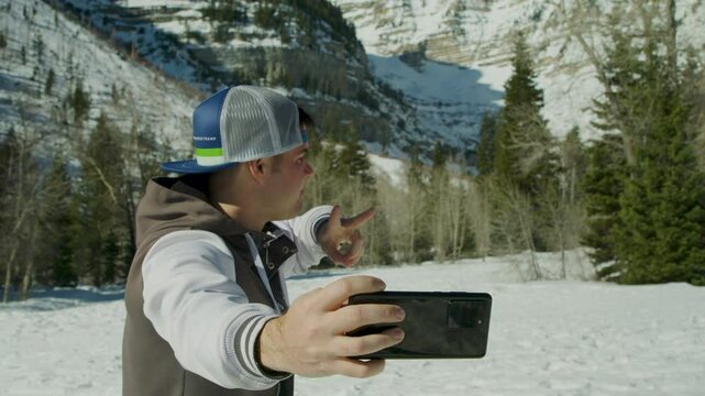 Man with backwards hat taking a selfie in snowy canyon, medium shot