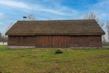 Obraz premium An ecological barn made of pure brown wood and a thatched roof on it, an authentic barn in a green yard amidst a blue sky, a place of strength and tranquility, a bird's nest on the roof of the barn.