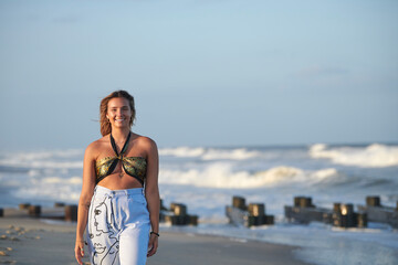 Fototapeta premium Beautiful young blonde woman walks along beach at sunset