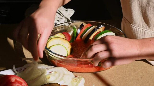 Woman Preparing a Ratatouille Dish with Roasted Vegetables in a Glass Casserole