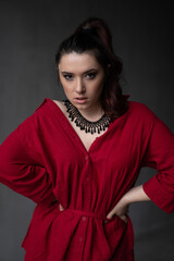 a beautiful young girl in a red shirt with a necklace with a handmade ornament on her neck is posing in a photo studio