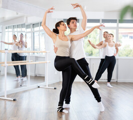 Obraz premium Young guy and adult woman perform paired ballet dance in studio