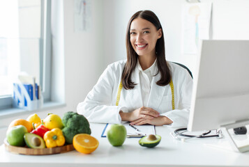 Young European dietitian working in office with computer, making balanced corrective diet plan for...