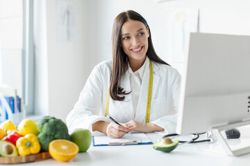 Nutritionist doctor writing diet plan and using computer, having online consultation with patient,...
