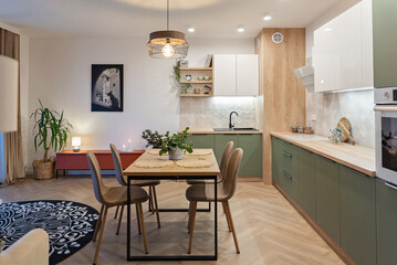 Modern kitchen interior with table and chairs. Green and white furniture with cabinet, beige tiles and picture on the wall. Design in new apartment. Real estate.	