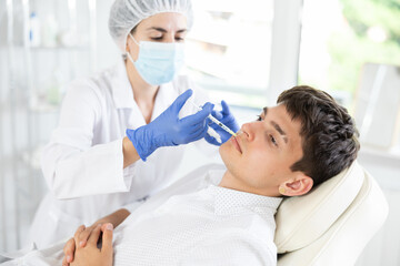 Fototapeta premium Young man having face mesotherapy implemented by middle-aged dermatologist in aesthetic clinic