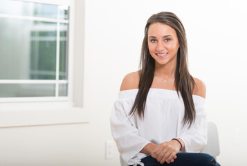 Stunning young Caucasian woman sits in small wooden chair in empty room