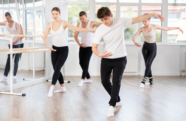 Fototapeta premium Motivated sporty young guy participating in group ballet class, practicing graceful dance movements in sunlit choreography studio ..