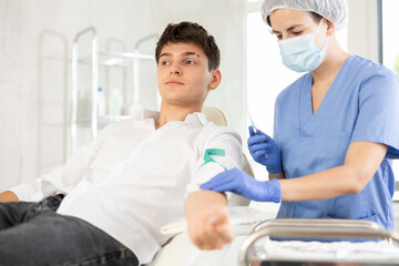 Fototapeta premium Nurse giving intravenously injection to young brown-haired boy lying at exam room of clinic