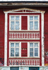 Red and white facade with windows of an abandoned wooden building.