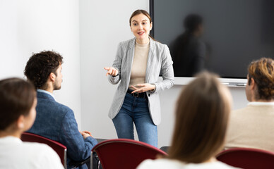 Young female professor explaining subject to classroom full of students