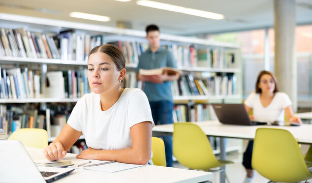 Caucasian school student girl doing research on project laptop in the college library