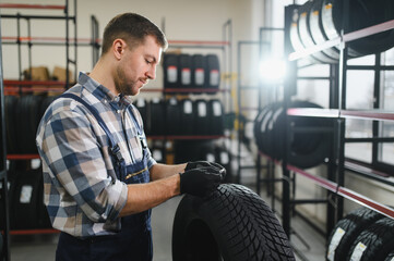 Portrait man mechanic holding new tyre on background store, car tire service concept