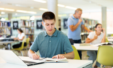 Positive young man in casual clothes working remotely using a computer in a quiet library