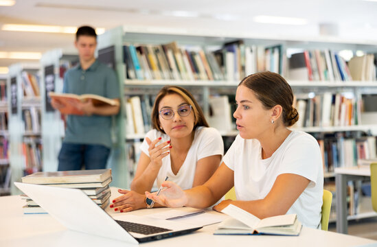 Skilled female students research laptop homework together in library