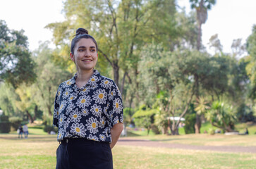 Happy woman enjoying a sunny day in the park. Smiling young woman in a floral shirt enjoying a sunny day outdoors in a lush green park.