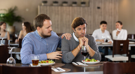 Two friends meeting in a modern restaurant - man comforts his upset sad friend